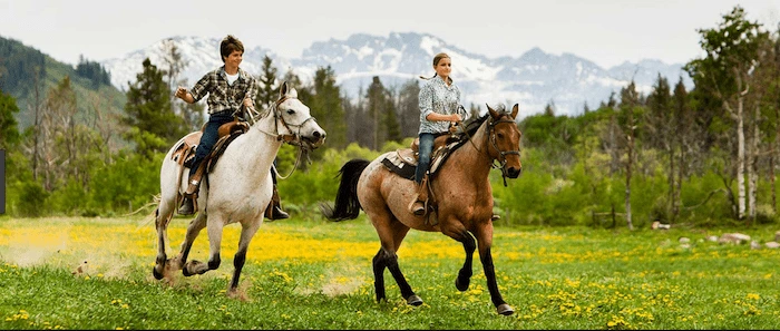 Confident plus-size woman riding Heath a horse through a field with a smile on her face.